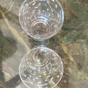 May include: Two clear glass tumblers viewed from above, each featuring a repeating white pattern of golf clubs, golf balls, and tees printed around the exterior surface of the cylindrical vessels with open circular rims.