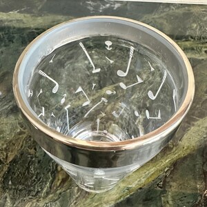 May include: A clear glass tumbler featuring a metallic silver rim and a white etched pattern of golf clubs, golf balls, and golf tees scattered across the exterior surface. The glass has a tapered cylindrical shape with a smooth, transparent finish.