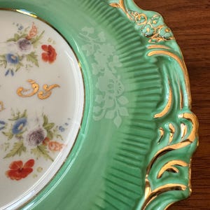 May include: A close-up of a decorative plate with a mint green rim and a white center. The rim has a textured design with gold accents. The center features a floral pattern with red, blue, and purple flowers.