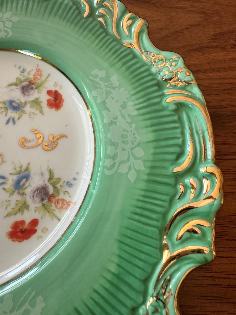 May include: A close-up of a decorative plate with a mint green rim and a white center. The rim has a textured design with gold accents. The center features a floral pattern with red, blue, and purple flowers.