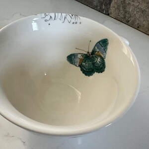 May include: White ceramic bowl with a butterfly design. The butterfly has teal and blue wings with a detailed pattern. The bowl has a smooth, glossy finish and a simple, elegant design.