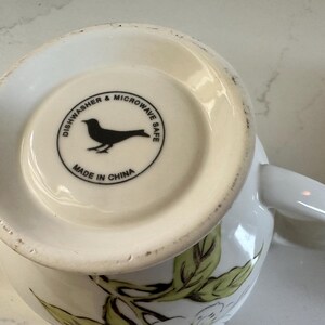 May include: White ceramic mug with a floral design and a handle. The bottom of the mug features a black bird silhouette inside a circle with the text "Dishwasher & Microwave Safe" and "Made in China".