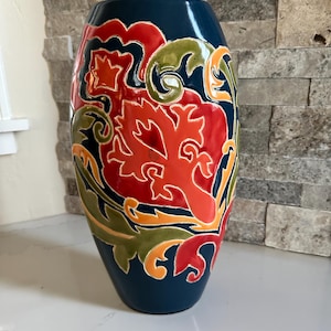 May include: A navy blue ceramic vase with a glossy finish. The vase features a vibrant floral design in red, orange, and green. The design is set against a dark blue background, creating a striking contrast. The vase is a decorative item.