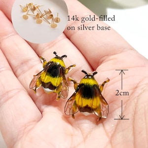 Peut inclure: Une paire de boucles d'oreilles en forme d'abeille en or rempli sur une base en argent. Les boucles d'oreilles mesurent 2 cm et présentent un motif d'abeille détaillé avec des rayures noires et jaunes.