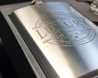 May include: A silver flask with a black box. The flask has an engraved design that says "Best Premium Quality" and "Luxury Est. 2024".