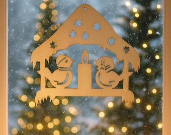 May include: A wooden Christmas decoration with a bird and dog silhouette design, a candle, and star cutouts hangs in front of a window. Five red pillar candles with lit flames are in the foreground. The background shows a snowy scene with blurred lights.