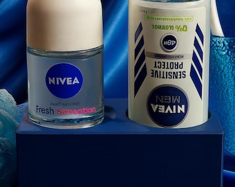 May include: Two Nivea deodorant products on a blue surface. One is a roll-on with a white cap and the text "Fresh Sensation". The other is a cylindrical deodorant stick with the text "Sensitive Protect Men". A blue bath sponge is also visible.