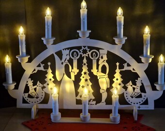 May include: A white wooden Christmas candle bridge with nine LED candles. The bridge features cut-out silhouettes of angels, Christmas trees, and other festive figures. The candles are arranged in an arch shape, creating a warm, inviting glow.