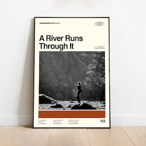 Puede incluir: Un póster enmarcado con el título "A River Runs Through It". El póster presenta una imagen en blanco y negro de una persona pescando con mosca en un río. El póster tiene un fondo crema con una franja marrón y naranja en la parte inferior.