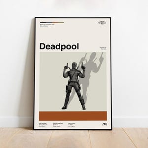 May include: Black framed poster featuring the word "Deadpool" in bold letters. The poster displays a grayscale illustration of the Deadpool character holding two guns, with his shadow behind him. The poster has a beige background with a brown stripe at the bottom.