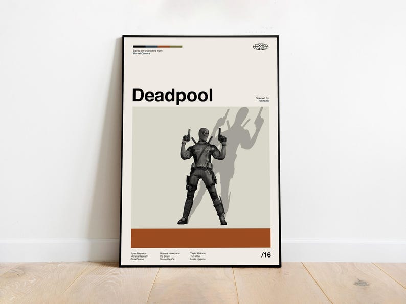 May include: Black framed poster featuring the word "Deadpool" in bold letters. The poster displays a grayscale illustration of the Deadpool character holding two guns, with his shadow behind him. The poster has a beige background with a brown stripe at the bottom.