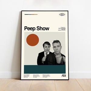May include: A framed poster featuring the text "Peep Show" in bold black letters. The poster includes two men, a large orange circle, and a teal rectangle. The poster is on a white wall and a wooden floor.