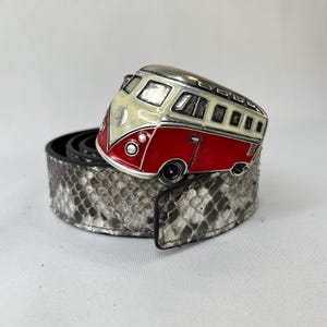 May include: A belt featuring a silver-coloured buckle in the shape of a red, cream, and silver vintage van. The belt is made of a snakeskin-patterned material.
