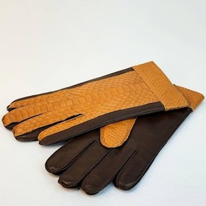 Könnte beinhalten: Ein Paar braune Lederhandschuhe. Die Oberseite der Handschuhe und die Manschetten weisen ein Schlangenmuster in hellem Braun auf. Die Handflächen und Finger sind in einem dunkleren Braun gehalten.