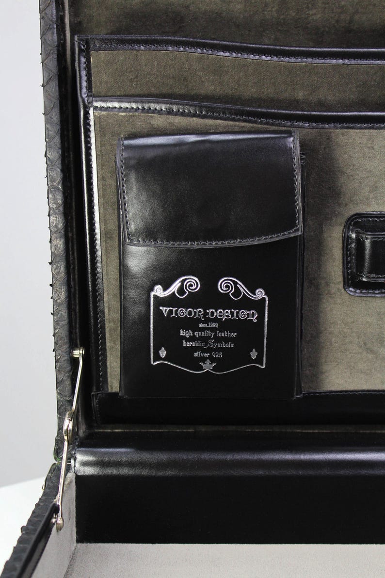 May include: Black leather briefcase with a silver clasp and a pocket with the text "VIGOR DESIGN" and the words "high quality leather". The interior is lined with a gray fabric.
