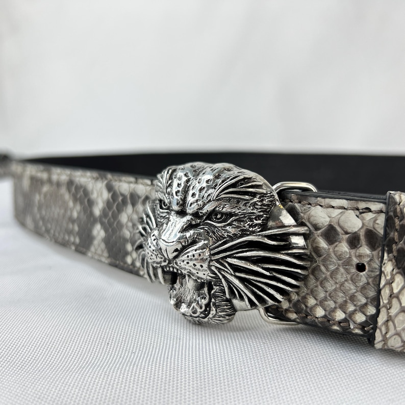Pode incluir: Uma fivela de cinto de metal prateado em forma de cabe&ccedil;a de jaguar rugindo &eacute; o ponto focal deste cinto. O pr&oacute;prio cinto tem um design de pele de cobra em tons de cinza e preto. Um acess&oacute;rio elegante.