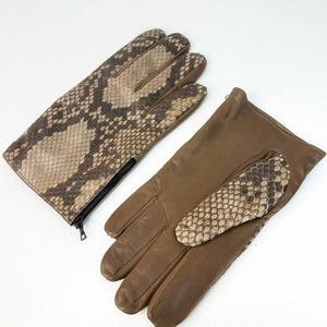 Op de afbeelding: Een paar bruin lederen handschoenen met slangenprint details. Eén handschoen heeft een volledig slangenprint ontwerp, de andere heeft een slangenprint patch. De handschoenen hebben een ritssluiting en staan tegen een witte achtergrond.