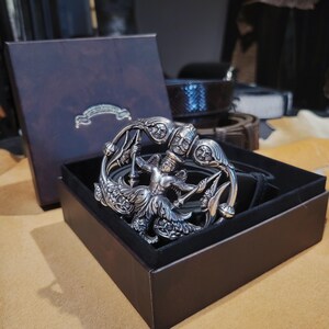 May include: A white ceramic mug with a black handle and the text "But First, Coffee" in a bold, black font. The mug is set against a neutral background, highlighting its simple design.