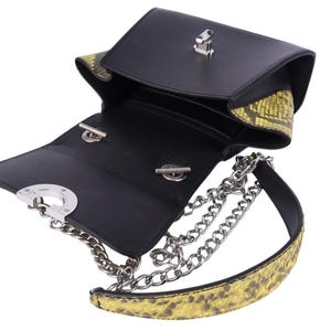May include: Black leather crossbody bag with a silver chain strap and yellow snakeskin-patterned accents. The bag has a flap closure with a silver clasp and a structured design. The interior is black.