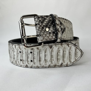 May include: A white and gray snakeskin belt with a silver-colored buckle. The belt has a black interior and is made of a textured material. The buckle is a double-prong style. The belt is a fashion accessory.
