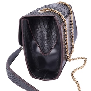 May include: Black leather handbag with a snakeskin texture. It has a gold chain strap and a matching snakeskin strap. The interior is black with red stitching. The bag is open, showing the inside.