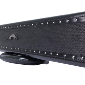 May include: Black leather cue stick case with a textured center panel and silver-colored rivets along the edges. The case has a decorative metal clasp and a curved, padded base.