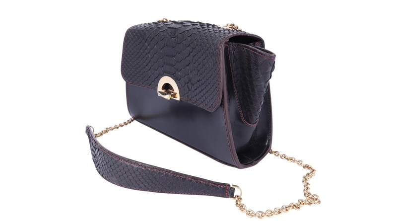 May include: A dark brown leather handbag with a textured flap and a gold-coloured clasp. The bag features a gold chain strap and a matching textured leather shoulder strap. The bag is set against a white background.