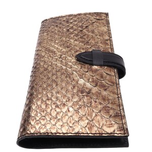 Może przedstawiać: Portfel ze skóry węża w kolorze złotym z czarnym paskiem skórzanym i klamrą.