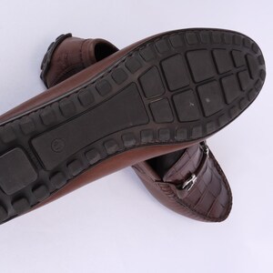 May include: Brown leather loafers with a textured crocodile pattern on the vamp. The soles are dark brown with a rubber tread. The shoes are designed for comfort and style.