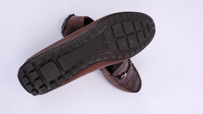 May include: Brown leather loafers with a textured crocodile pattern on the vamp. The soles are dark brown with a rubber tread. The shoes are designed for comfort and style.