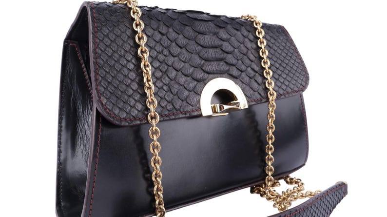 May include: Black leather handbag with a textured flap and a gold chain strap. The bag features a gold-coloured clasp and a contrasting red stitch detail. The design incorporates a snakeskin pattern on the flap.