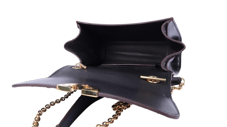 May include: Black leather handbag with a gold chain strap and clasp. The bag is open, revealing a dark interior. The edges are trimmed with brown leather. The bag has a unique, angular shape.