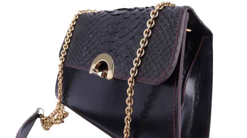 May include: Black handbag with a textured flap and a gold chain strap. The bag features a gold clasp and red stitching. The body of the bag is a glossy black, and the flap has a snakeskin pattern.