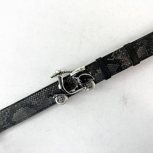 May include: A black and gray snakeskin-patterned belt with a silver-colored scooter buckle. The scooter buckle has black accents and detailed wheels. The belt is made of a textured material and has a classic buckle closure.