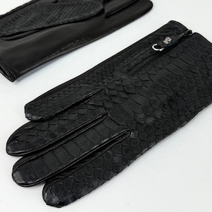 Peut inclure: Gants en cuir noirs avec une texture peau de serpent. L'un des gants présente une fermeture éclair au poignet. Les gants sont conçus dans un style classique à cinq doigts, offrant un look élégant.