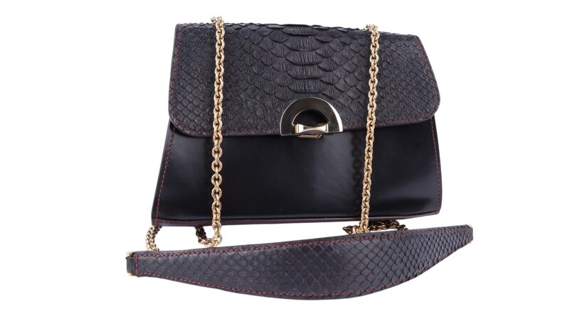 May include: Black handbag with a textured flap and a gold chain strap. The bag has a sleek, rectangular design with a contrasting smooth leather body. The strap and flap have a reptile-like pattern. A gold-tone clasp secures the bag.