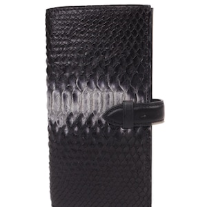 May include: A black leather wallet with a textured, snake-skin pattern. The wallet has a flap closure with a small, black leather strap and buckle. The wallet is rectangular and appears to be closed.