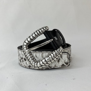 Może przedstawiać: Biało-szary pasek ze wzorem skóry węża ze srebrną klamrą. Pasek ma czarne skórzane oparcie i srebrną metalową klamrę z dekoracyjnym wzorem.