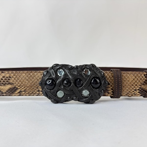 May include: A brown snakeskin-patterned belt with a decorative black buckle. The buckle features a geometric design with black and clear gemstones. The belt has a leather backing and a brown leather strap.