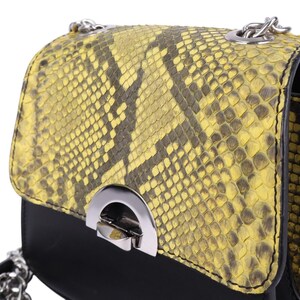 May include: A small, black and yellow snakeskin-patterned handbag with a silver chain strap. The bag features a flap closure with a silver clasp. The snakeskin pattern is a mix of yellow and dark brown.