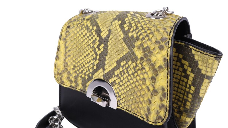 May include: A small, black and yellow snakeskin-patterned handbag with a silver chain strap. The bag features a flap closure with a silver clasp. The snakeskin pattern is a mix of yellow and dark brown.