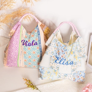 May include: Two patchwork tote bags with floral and patterned fabric. One bag has the name "Viola" embroidered in purple, the other has "Elisa" in blue. Both bags have pink handles.