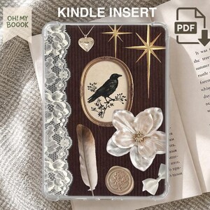 May include: A rectangular Kindle insert featuring a dark brown corduroy background with a white lace border. The design includes a gold-framed crow illustration, a heart pendant, gold stars, a feather, a white flower, a wax seal, and a small bow.