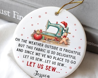May include: White ceramic Christmas ornament with a sewing machine, tomato, gingerbread man, and text. The text reads "Oh the weather outside is frightful but this fabric is so delightful and since we've no place to go let us sew..." with a name below.
