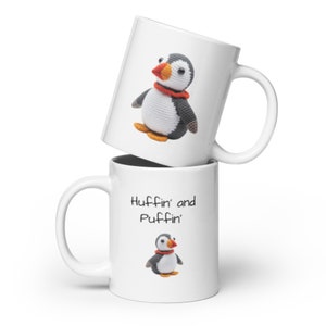 May include: White ceramic mug with a black and white illustration of a puffin with an orange beak and red scarf. The mug has the text "Huffin' and Puffin'" printed on it.