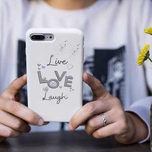 Pode incluir: Capa branca para iPhone com um design brilhante e as palavras "Live Love Laugh" em letras cinzas.