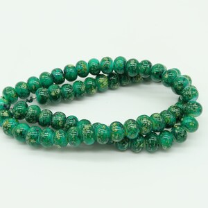 May include: A strand of green glass beads with gold flecks. The beads are round and have a slightly irregular shape.