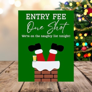 以下が含まれることがあります： 「ENTRY FEE One Shot」と「We're on the naughty list tonight!」というテキストが入った、緑色のクリスマスをテーマにしたサイン。サンタの足とブーツが煙突から突き出ている様子が描かれており、ショットグラスも写っています。背景にはクリスマスツリーがあります。
