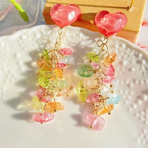 May include: A pair of dangle earrings featuring a heart-shaped charm at the top and a cascade of colourful, iridescent, faceted beads hanging below. The beads are in shades of pink, green, yellow, and blue.