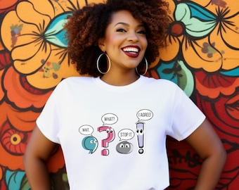 May include: A white t-shirt featuring cartoon speech bubbles with punctuation marks and the phrases "WAIT," "WHAT?," "STOP IT," and "I AGREE!". The shirt is worn by a person in front of a colorful floral mural.